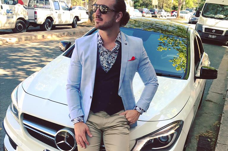 A man sits on the bonnet of a white Mercedes car.