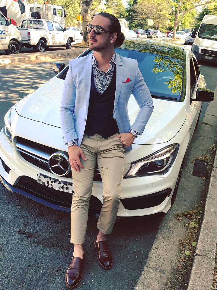 A man sits on the bonnet of a white Mercedes car.