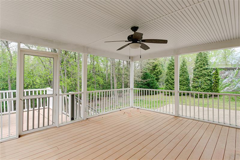Enclosed patio with white railings and ceiling fan overlooking a green courtyard.