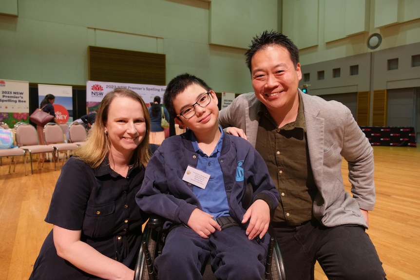 A young boy in a wheelchair smiling with his father and mother