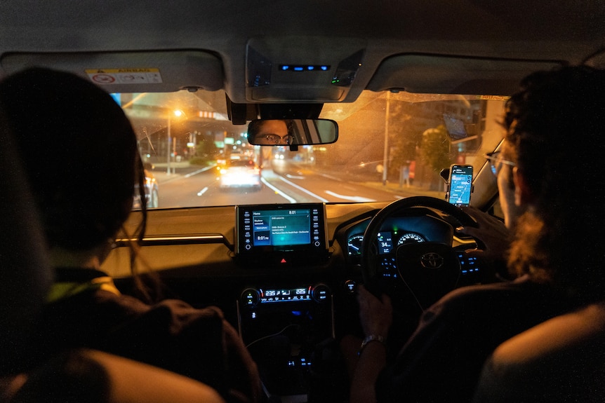 Two youth workers sit inside a car driving city streets