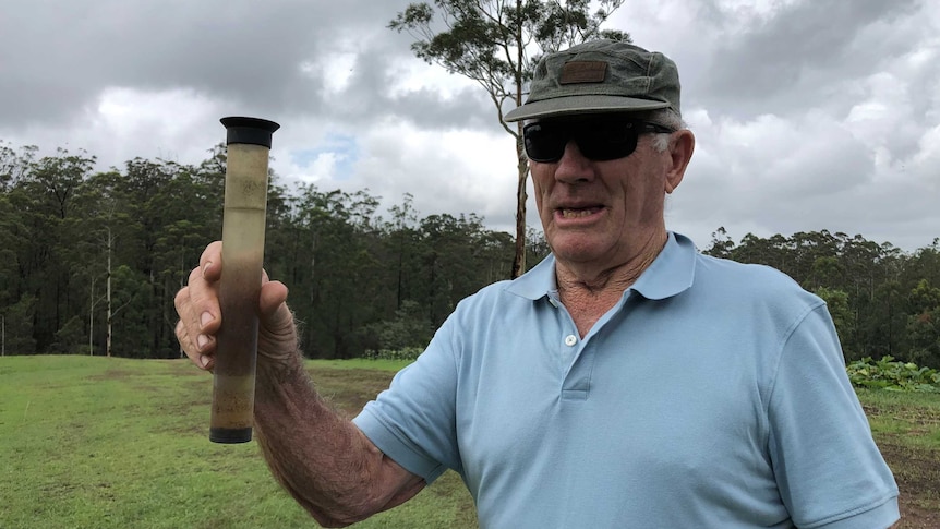 A man holds up an almost-full rain gauge.