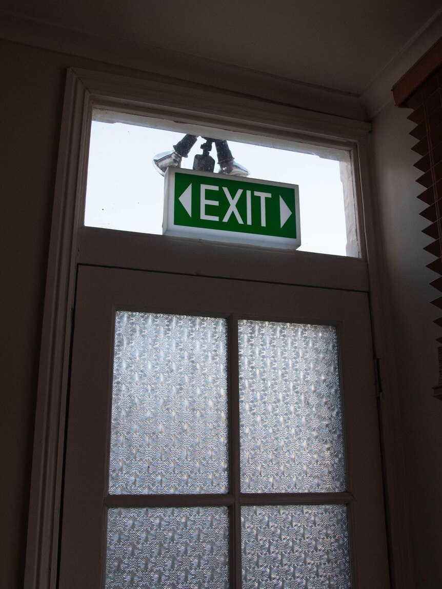 An exit sign positioned in front of a glass panel above a door with two glass inset windows