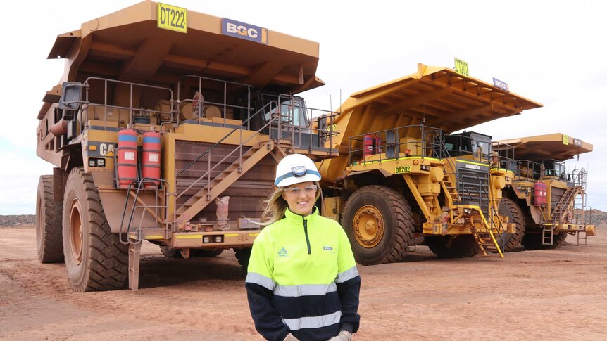 Woman in high vis gear standing in front of  three trucks in the middleground