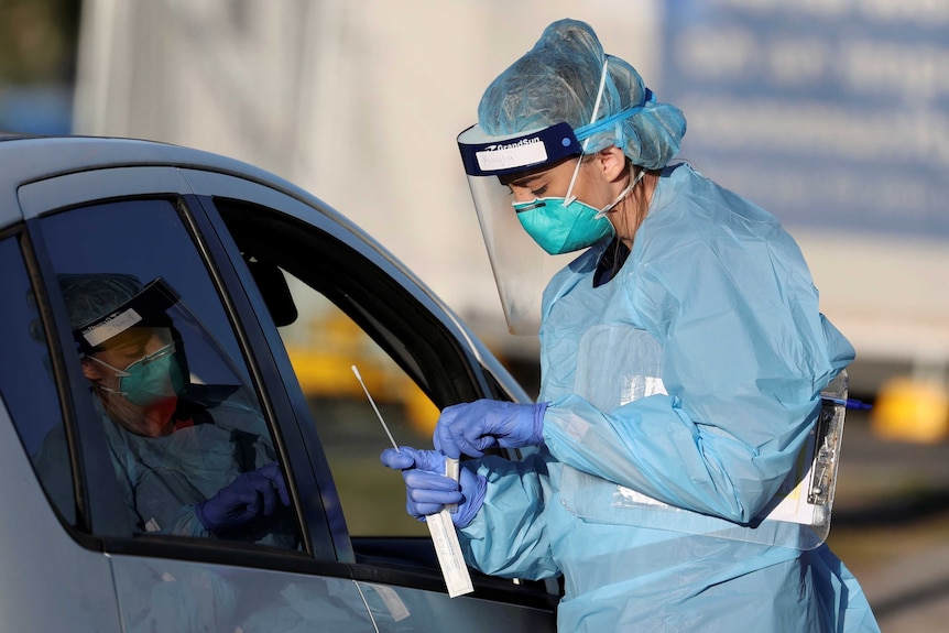 A woman in a blue uniform swabs a person through the car window