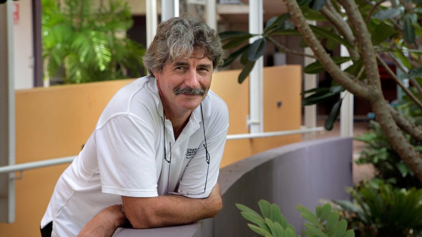 A man with a moustache and a white polo shirt leans on a ramp at Charles Darwin University.