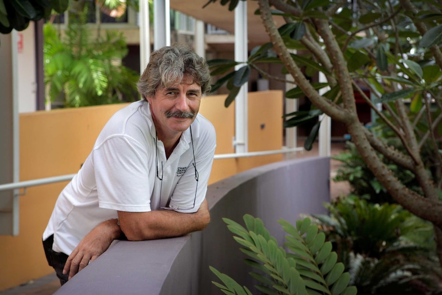 A man with a moustache and a white polo shirt leans on a ramp at Charles Darwin University.