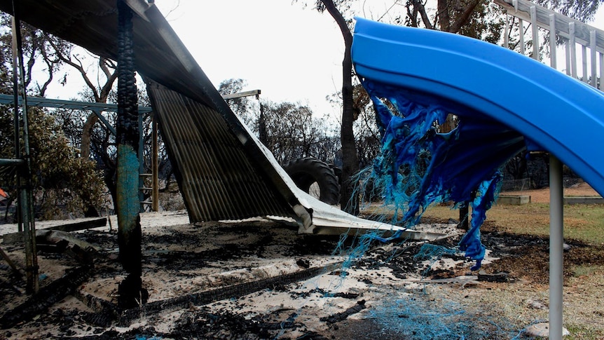 A partially melted blue plastic playground slide and twisted corrugated metal after a bushfire.