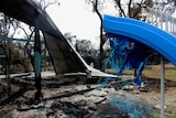 A partially melted blue plastic playground slide and twisted corrugated metal after a bushfire.