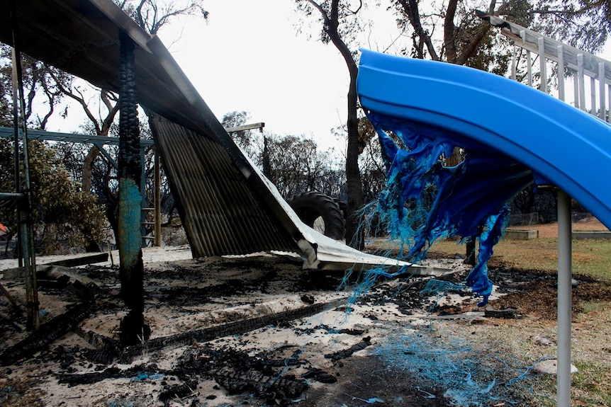 A partially melted blue plastic playground slide and twisted corrugated metal after a bushfire.