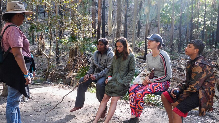 Aunty Mel stands on the far left speaking to three students and a supervisor in a rainforest at Carnarvon Gorge.