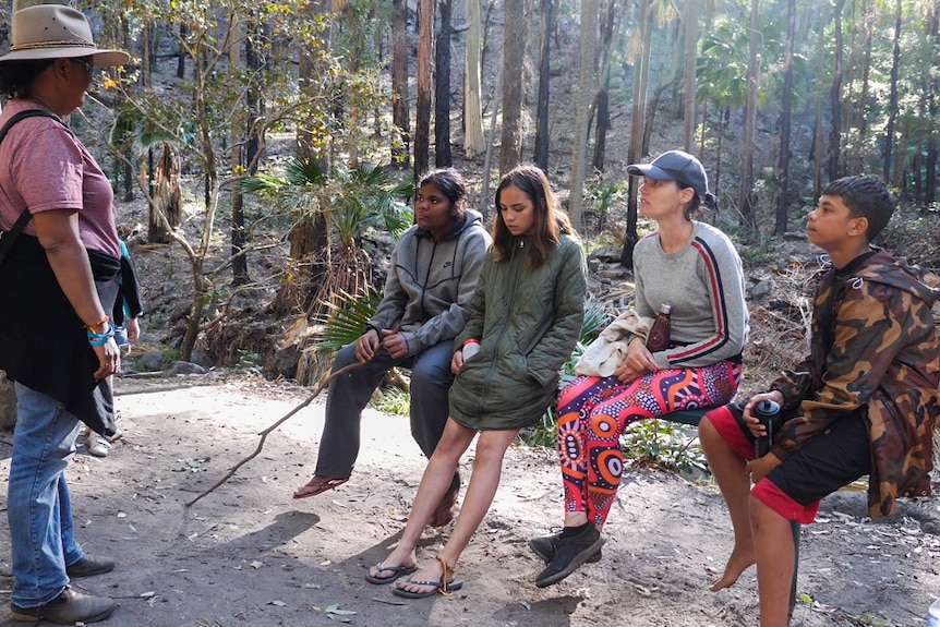 Aunty Mel stands on the far left speaking to three students and a supervisor in a rainforest at Carnarvon Gorge.