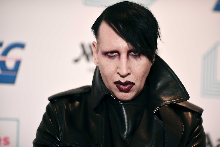 Musician Marilyn Manson is wearing dark eye makeup and lipstick and a black leather coat