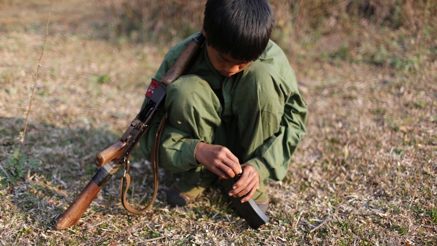 A 15-year-old child soldier in Myanmar loads a gun