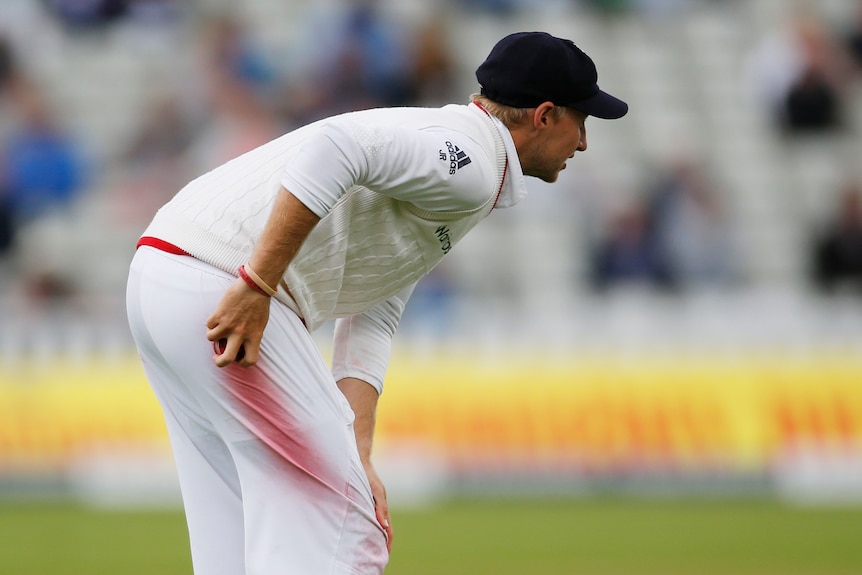 A cricket player wipes a red ball on his white trousers leaving a red skid mark