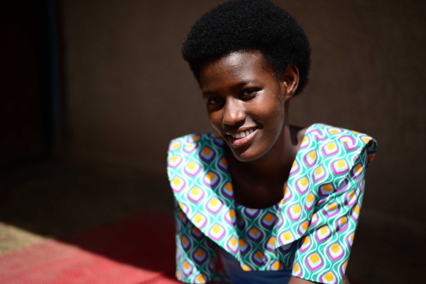 A young girl smiles while sitting down in a bright colourful dress