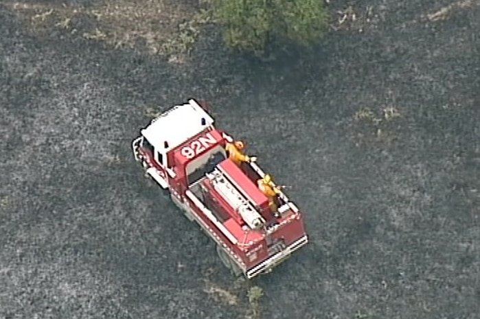 An aerial image of two firefighters standing on a fire truck on burnt ground at Benloch.