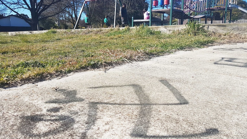 A swastika spray-painted on the footpath in front of a playground.