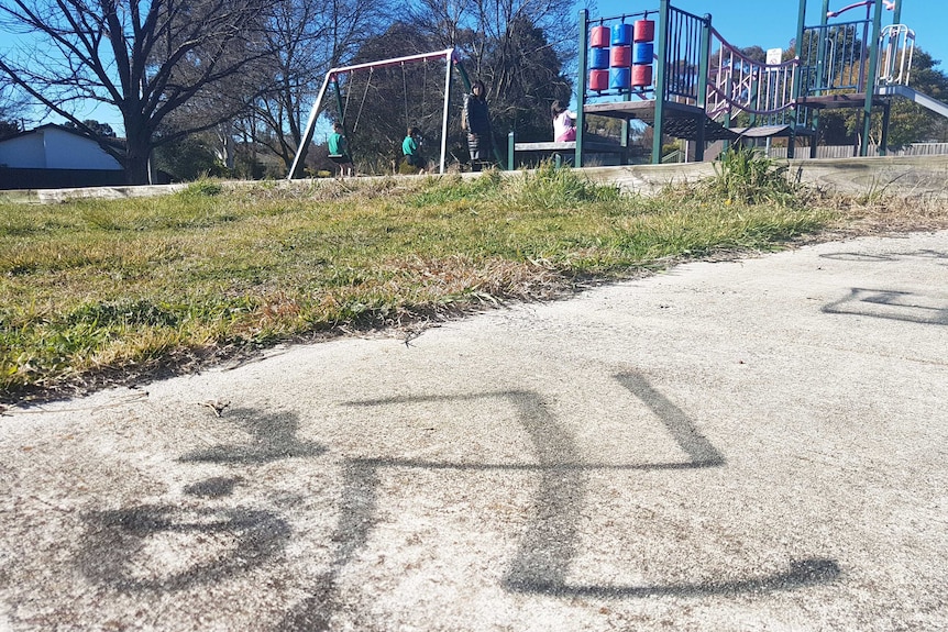 A swastika spray-painted on the footpath in front of a playground.