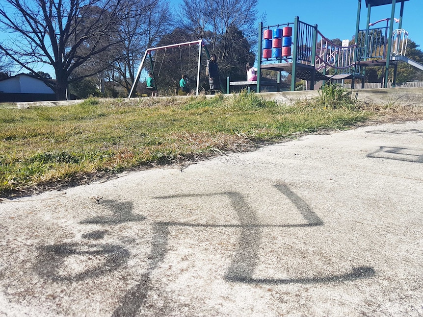 A swastika spray-painted on the footpath in front of a playground.