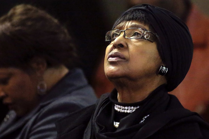 Winnie Madikizela-Mandela in black clothes looks above her with a somber expression