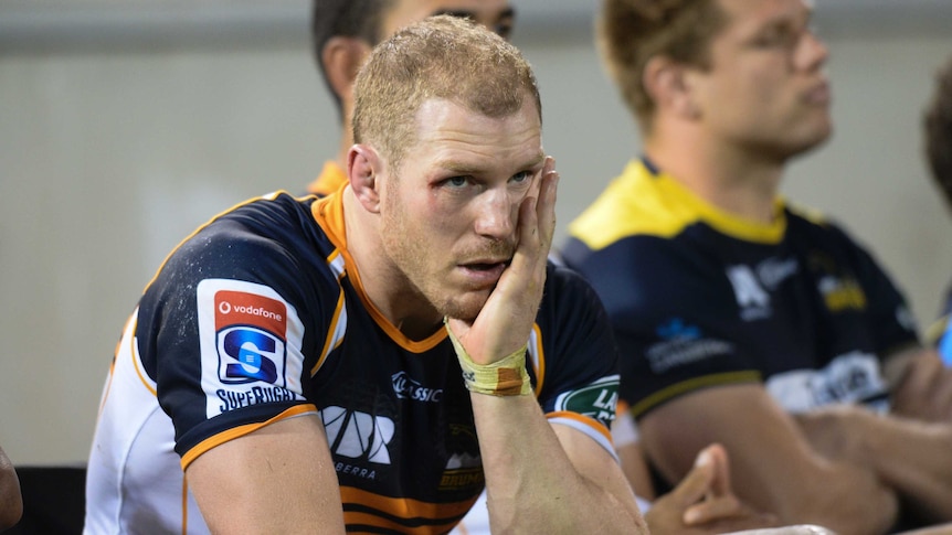 David Pocock sits on the bench in a Brumbies jersey with his head in his hand during a game.
