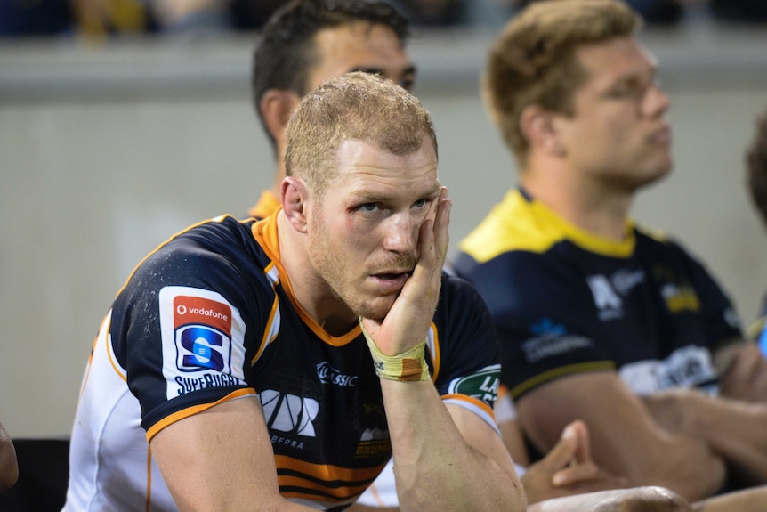 David Pocock sits on the bench in a Brumbies jersey with his head in his hand during a game.