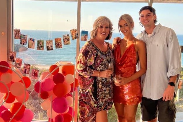 Kylie standing next to son and daughter at a party with a 21 sign made up of balloons beside them 