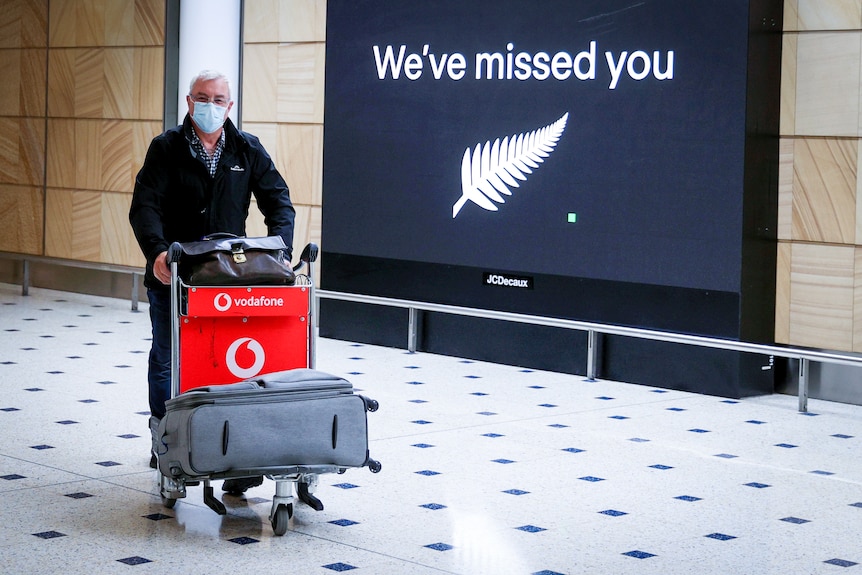 A man in a face mask pushes a cart of luggage past a sign reading "We have missed you" 