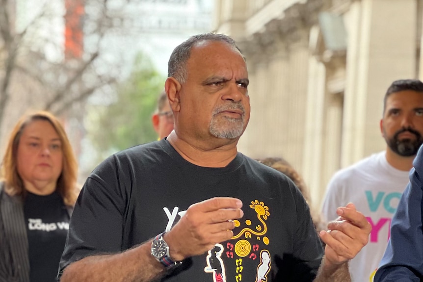 Michael Long gestures with his hands as he addresses a media conference in Melbourne wearing a 'Yes' t-shirt.