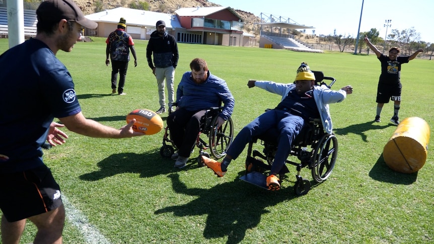 A coach holds a football during a drill with two young men with cerebral palsy