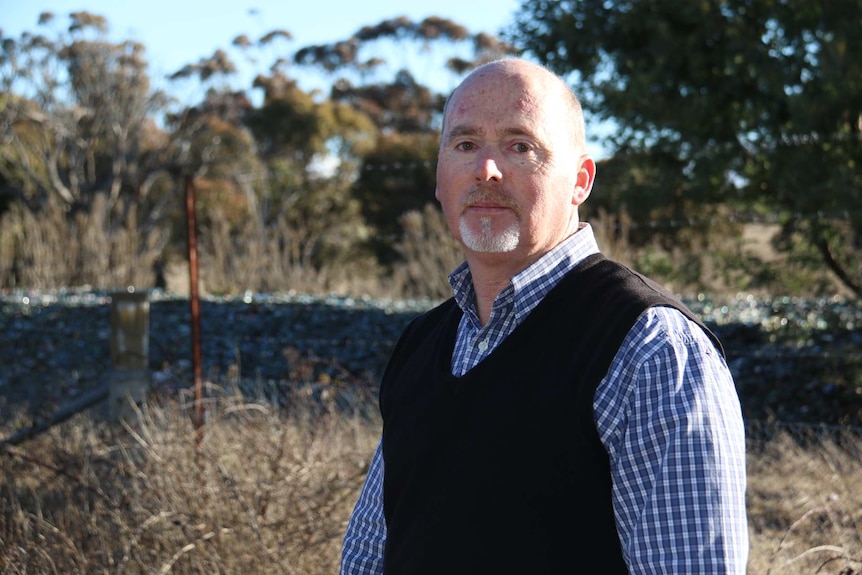 A man standing in front of a large pile of broken glass.