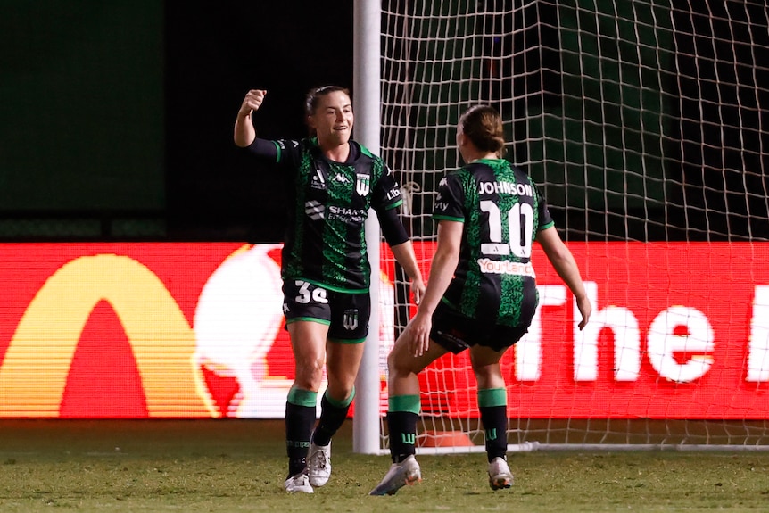 A soccer player wearing green and black celebrates with a team-mate after scoring a goal