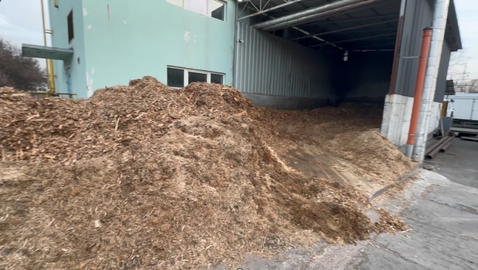Un montón de astillas de madera frente a la puerta abierta de una fábrica. 