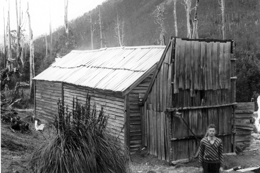 An unknown man stands in front of a rustic bush hut