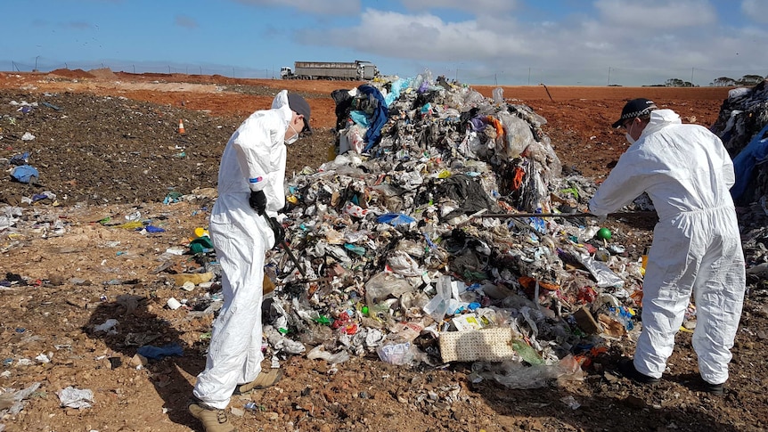 Two police officers scour a rubbish dump.