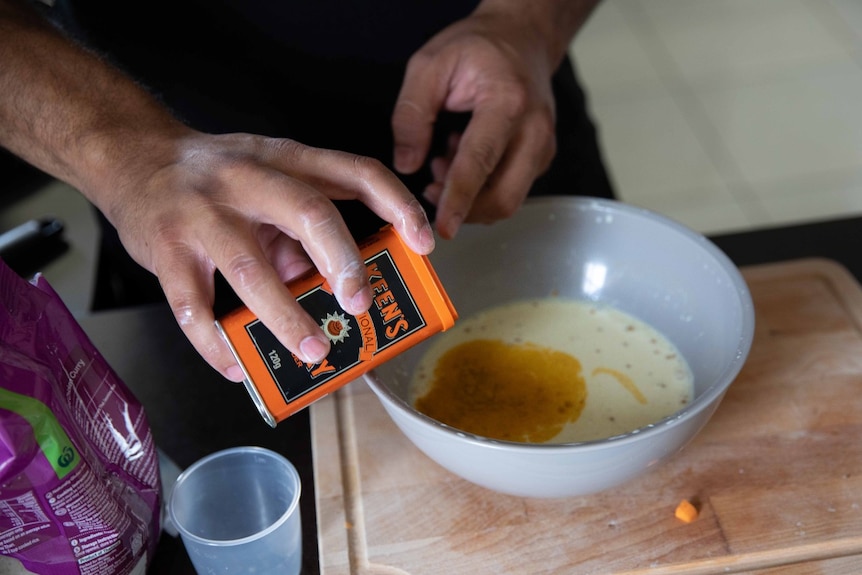 A pair of hands pours curry powder into a bowl of cream liquid