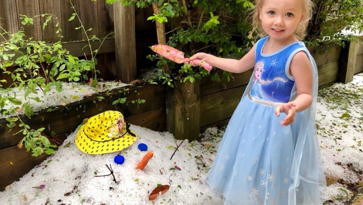 A little girl standing beside a pile of hail made to look like a head
