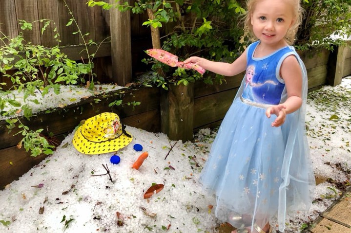 A little girl standing beside a pile of hail made to look like a head