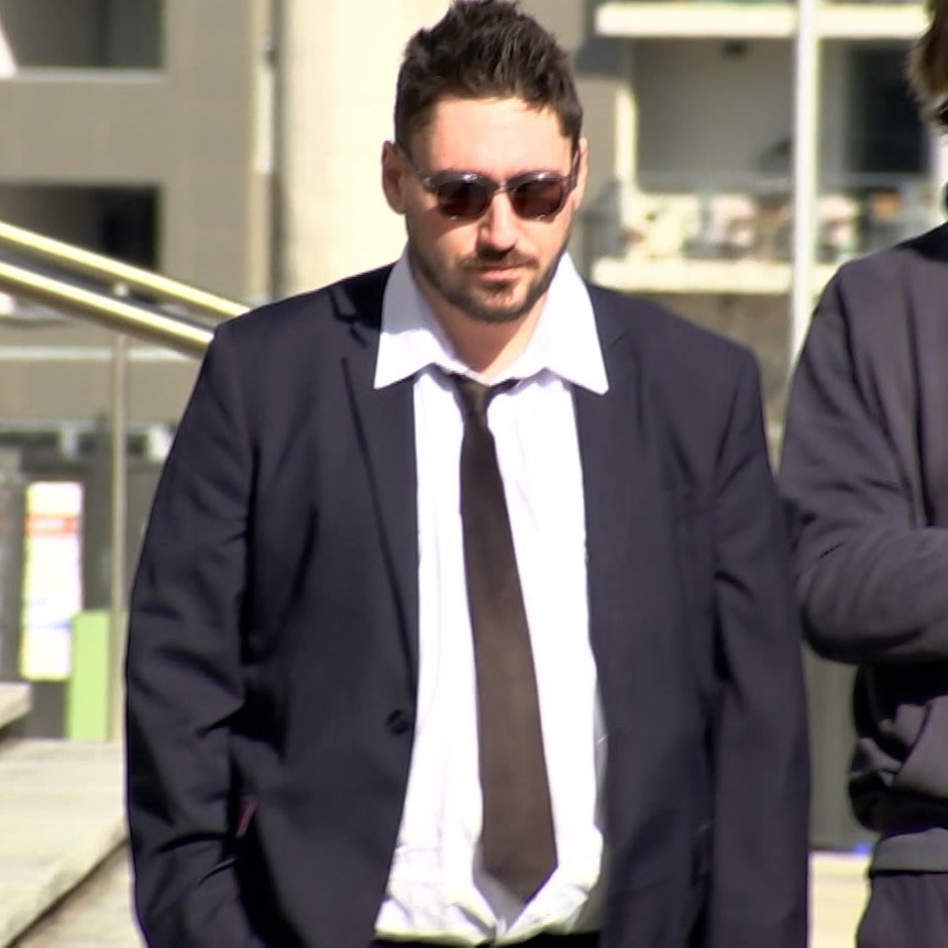 A man in a suit and tie walks with other men alongside him.