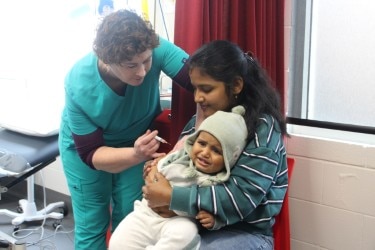 A woman holds her baby who's wearing a beanie