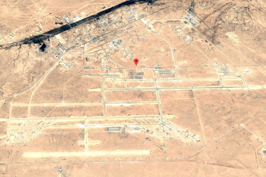 A satellite image of an airbase in a desert landscape with a creek running past it.