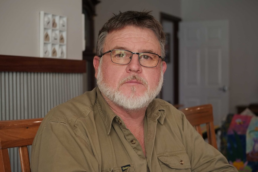 He sits in his living room, has glasses and a white beard