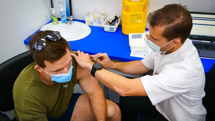 A pharmacist administers an vaccination into a mans upper arm