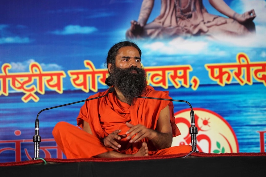 Yoga guru Baba Ramdev sits crossed-legged on a stage.