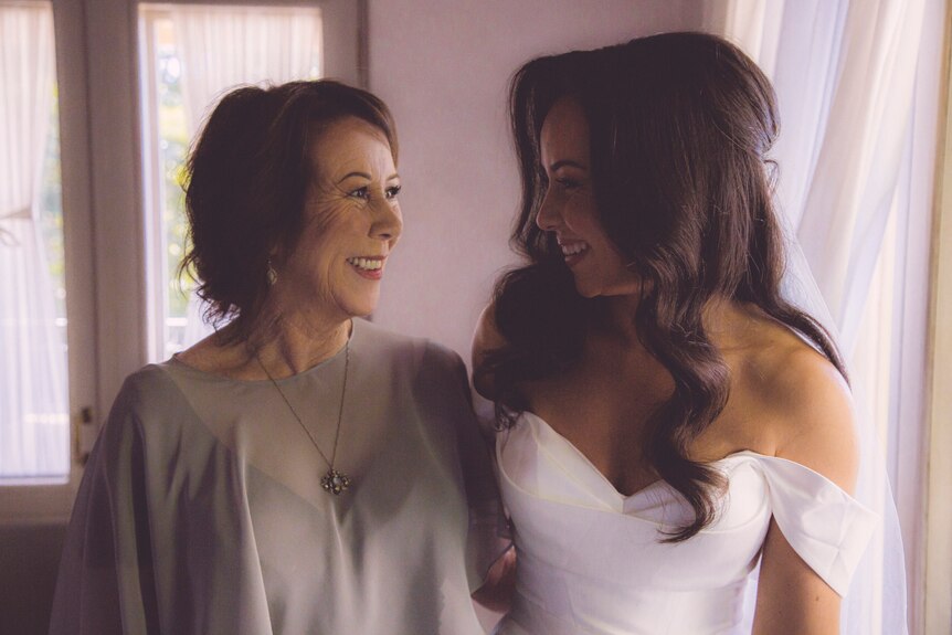 A bride with long dark hair smiles with an older woman with short brown hair
