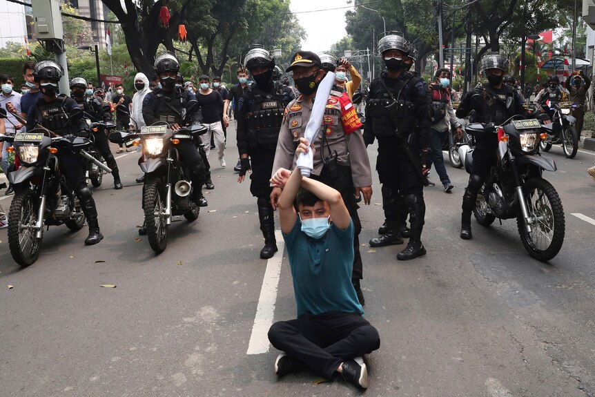 An Afghan refugee sits on the ground in front of Indonesian riot police in Jakarta