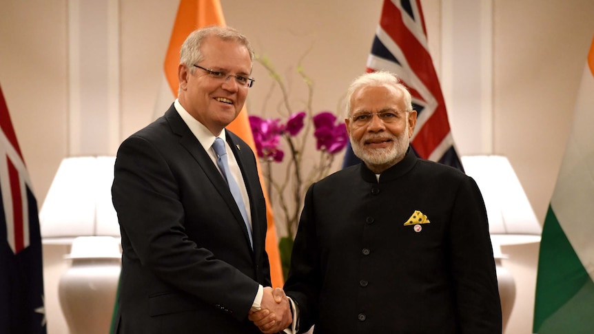 Scott Morrison, left, shakes hands with Narendra Modi, right, as they both look into the camera.