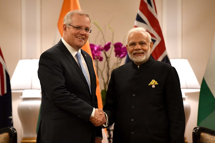 Scott Morrison, left, shakes hands with Narendra Modi, right, as they both look into the camera.