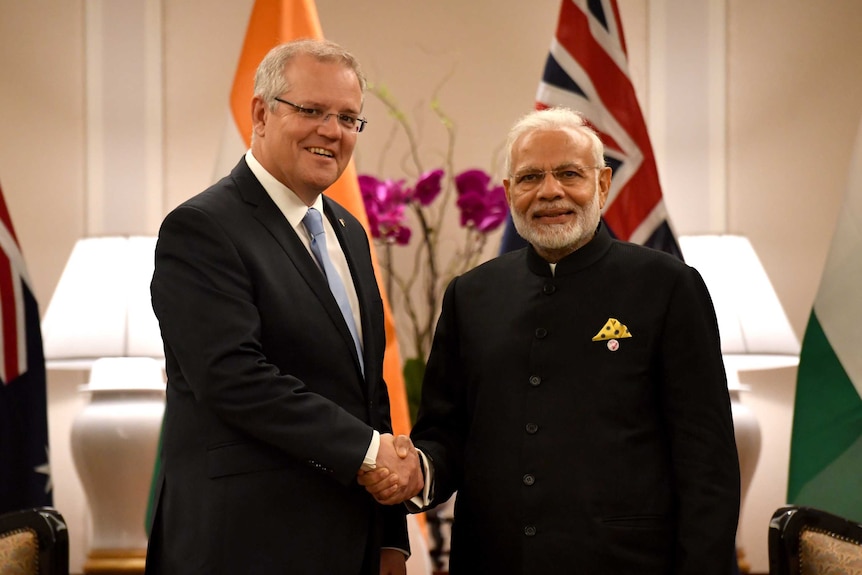 Scott Morrison, left, shakes hands with Narendra Modi, right, as they both look into the camera.
